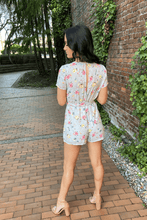 Load image into Gallery viewer, Take on the warm weather with this beautiful romper! This fully lined piece features short sleeves, wrap front, and tied waistline, with a zip closure in the back. The color is a light dusty blue with beautiful yellow and pink flowers. Looks great with a pair of flats for a casual look or even dress it up with a pair of heels. 100% Polyester Available in sizes Small, Medium, and Large Lined Button and zip back closure
