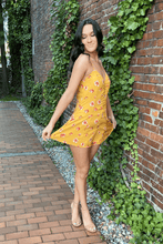 Load image into Gallery viewer, Slay them with sweetness when you show up wearing this floral romper!  Features adjustable spaghetti straps and a side zip closure.  The front buttons up for added style.  Darts are added for a beautiful fit.  The color is canary yellow with pink flowers.  Wear it with a pair of casual tennis shoes or dress it up with a pair of heels.    100% polyester  Available in sizes Small, Medium, and Large Adjustable straps Lined Side zip closure Darts
