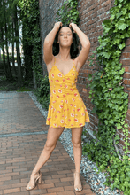 Load image into Gallery viewer, Slay them with sweetness when you show up wearing this floral romper!  Features adjustable spaghetti straps and a side zip closure.  The front buttons up for added style.  Darts are added for a beautiful fit.  The color is canary yellow with pink flowers.  Wear it with a pair of casual tennis shoes or dress it up with a pair of heels.    100% polyester  Available in sizes Small, Medium, and Large Adjustable straps Lined Side zip closure Darts
